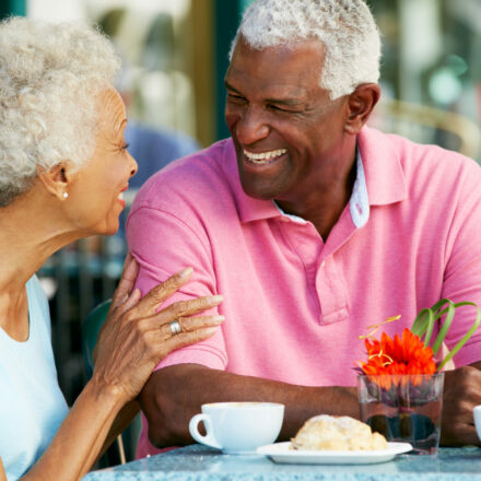Senior Couple Enjoying Snack At Outdoor Café Talking To Each Other Laughing